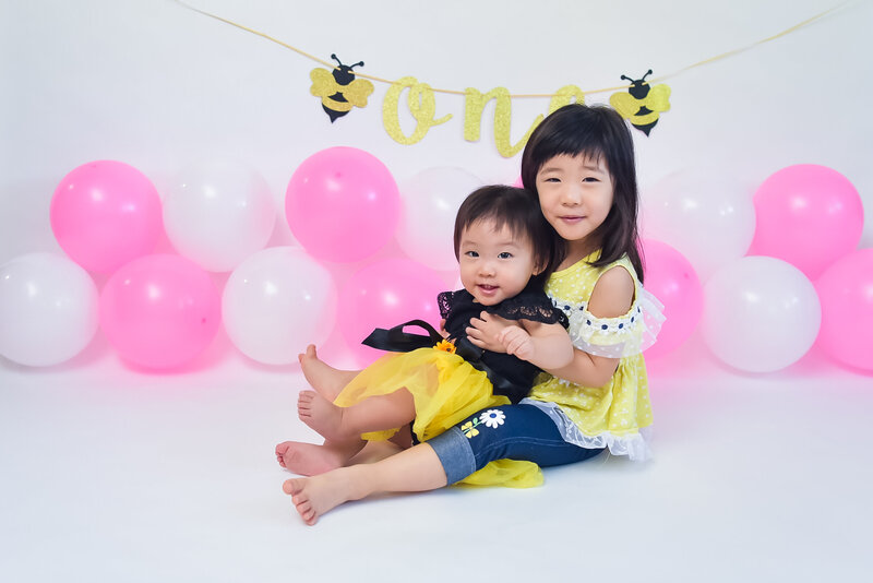 A one-year-old and her older sister at her cake smash photo session.
