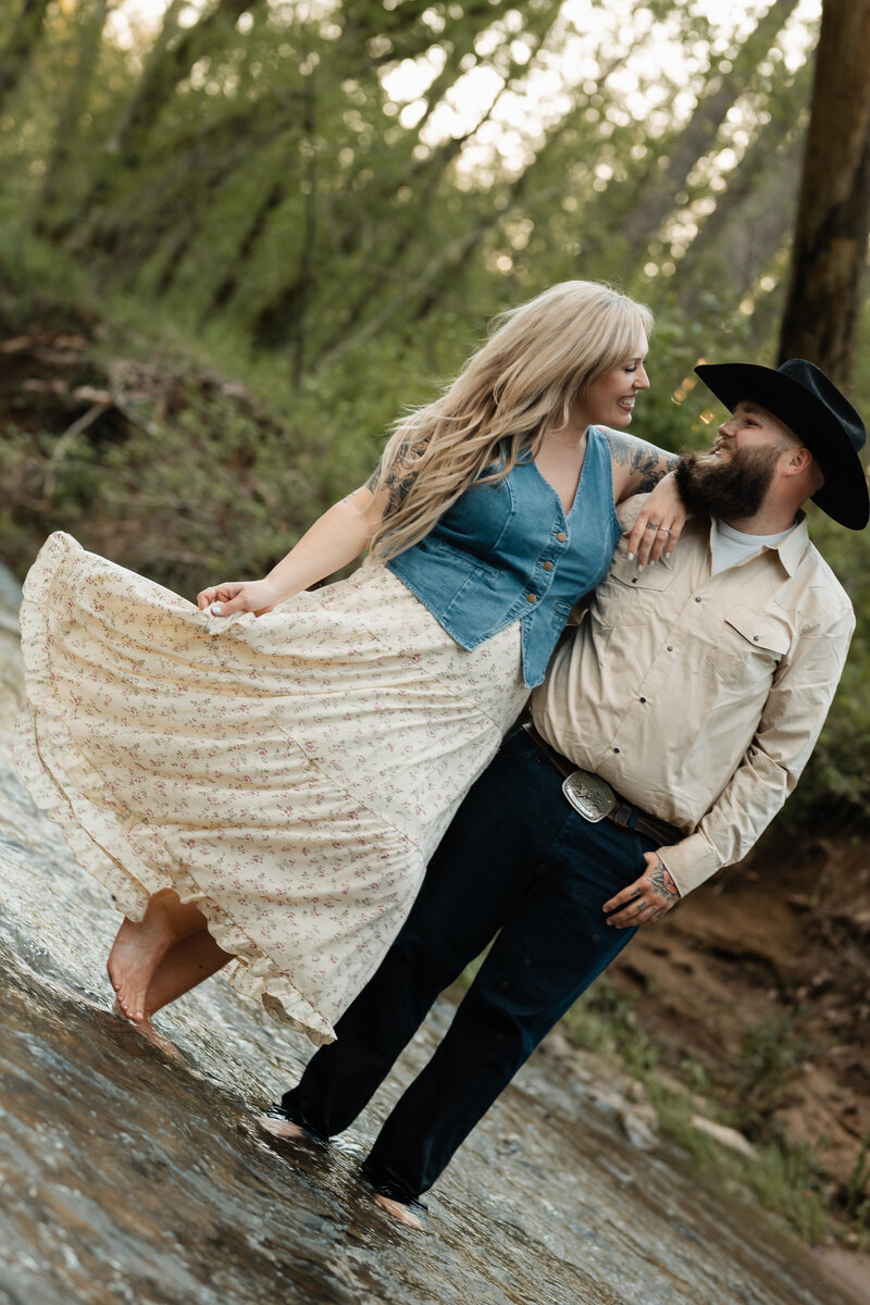 Couple sharing a tender moment near a creek, surrounded by nature, captured in a beautiful outdoor setting.