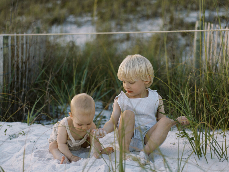 Two brothers playing in the sand together near the sea oats in Seaside, Florida.