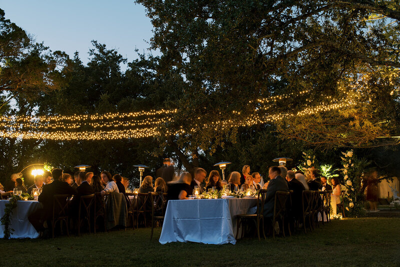 Guests enjoying a romantic outdoor wedding reception under twinkling string lights and surrounded by lush greenery, captured during an intimate evening celebration by Stephanie Michelle Photography, specializing in luxury weddings.