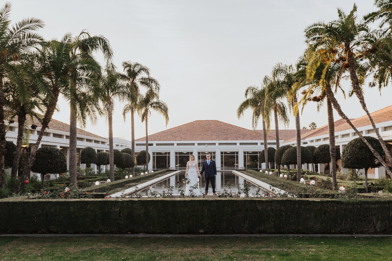 Wedding Photographer, bride and groom stand before large reflecting pool at resort