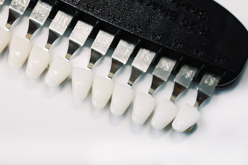 Shades of teeth samples arranged in a row, showcasing a gradient of colors from a natural white to a darker yellowish tone. Each sample is labeled with a number, representing different levels of whiteness, ranging from a bright, pearl-like white to a more off-white or slightly yellow shade. The samples are presented in a clear tray or holder, often used by dental professionals to assess the color of teeth for whitening treatments or cosmetic purposes.