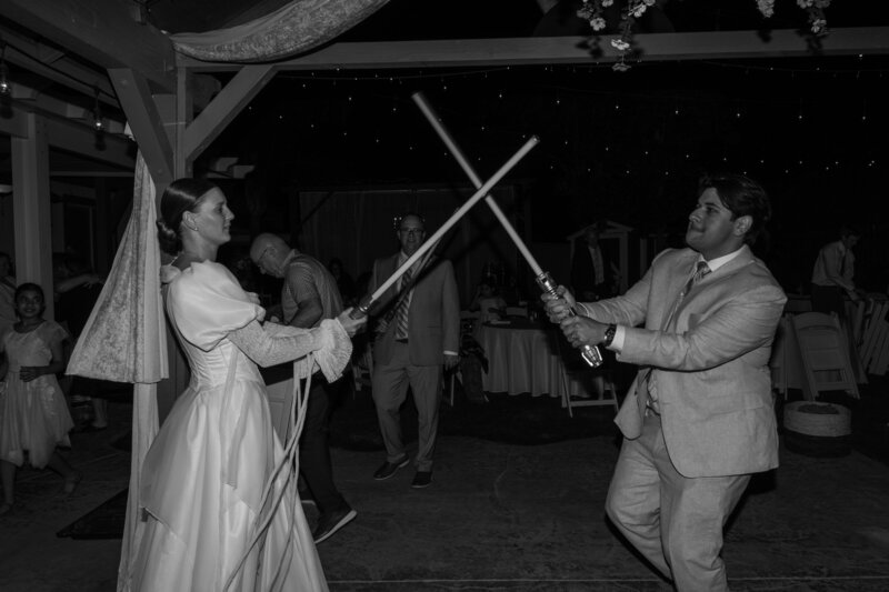 Regan & Yered dueling with lightsabers during their wedding reception. In black and white