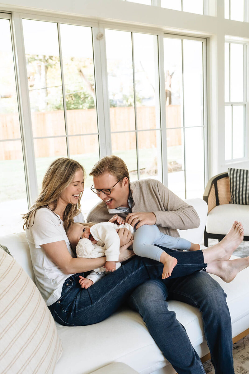 Health and wellness coach for moms sitting on the couch with her husband and toddler, enjoying a joyful family moment—real-life wellness for moms in early motherhood.