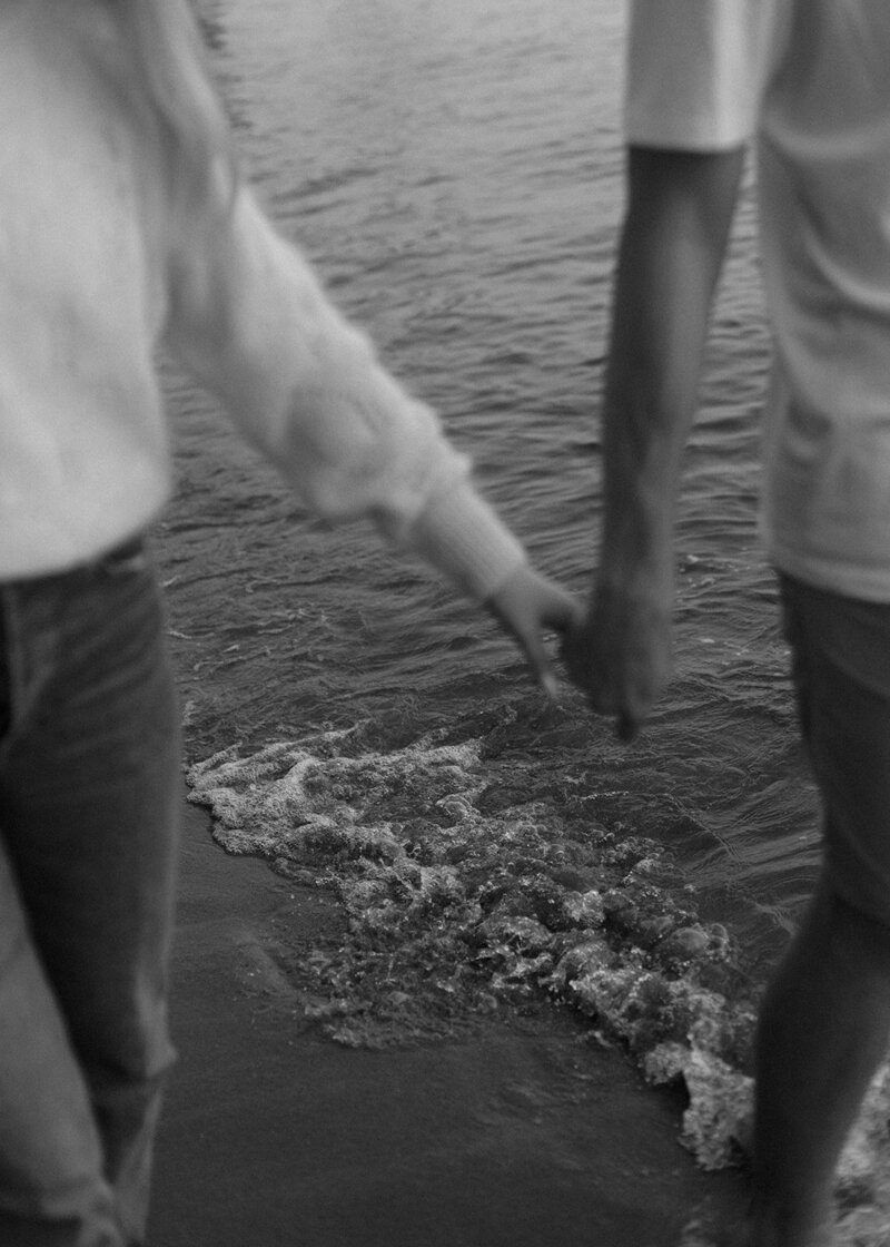 couple holding hands walking by the water