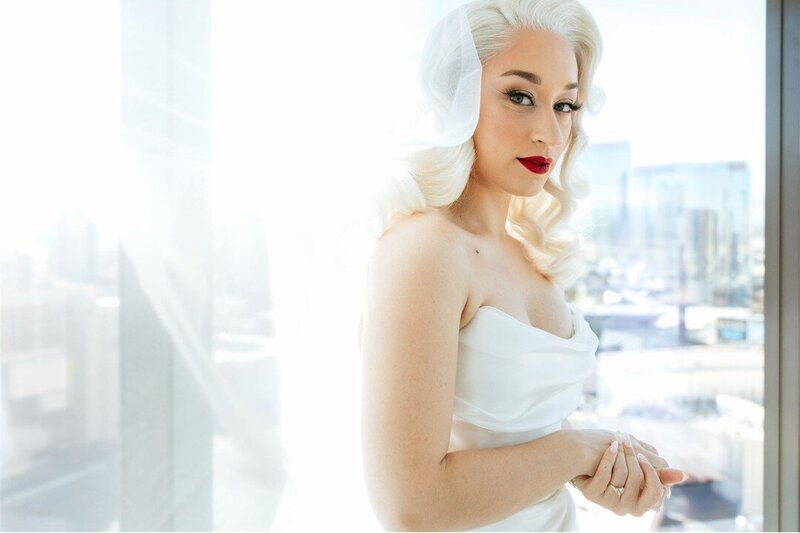 Stunning Bride in a classic white wedding dress with platinum blonde Hollywood wave hair, red lipstick in front of a window looking at the Las Vegas Strip.  Photography by Going Home Co.