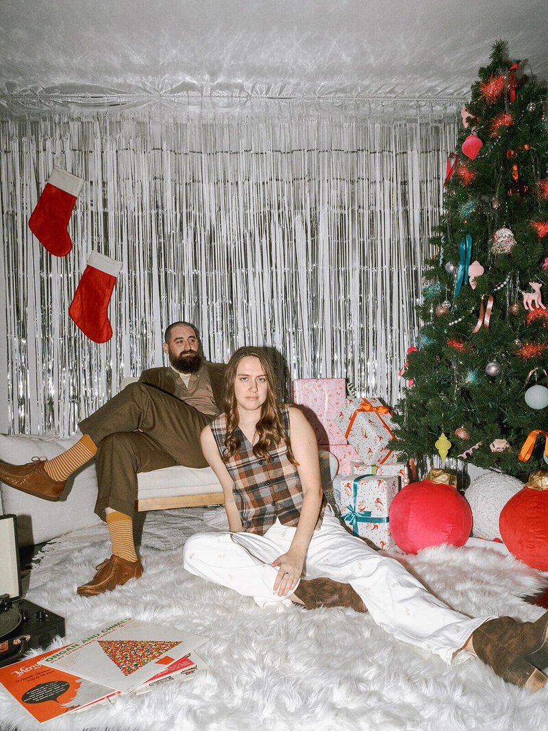 A couple sitting down at a styled photoshoot with Christmas decor. 