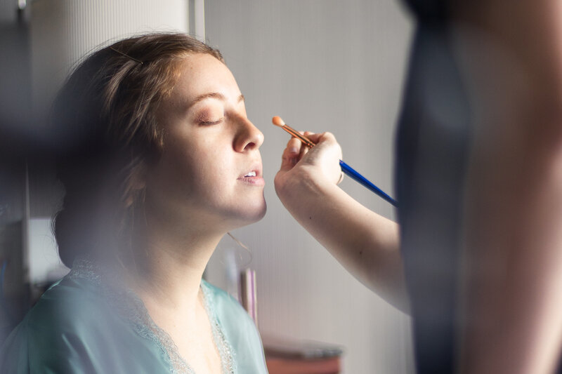 An image of a woman in a blue top getting eyeshadow applied