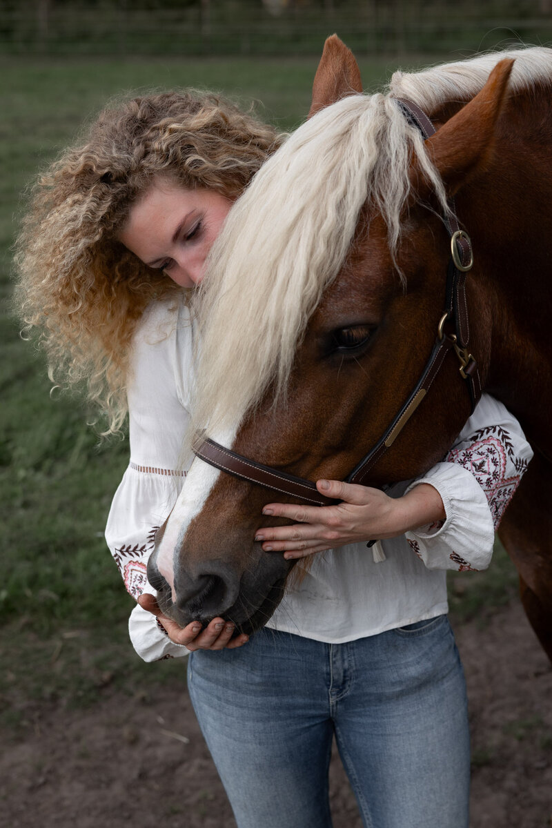 Liefdevol contact tussen Nikki Kleefman en haar paard in de groene paardenwei.