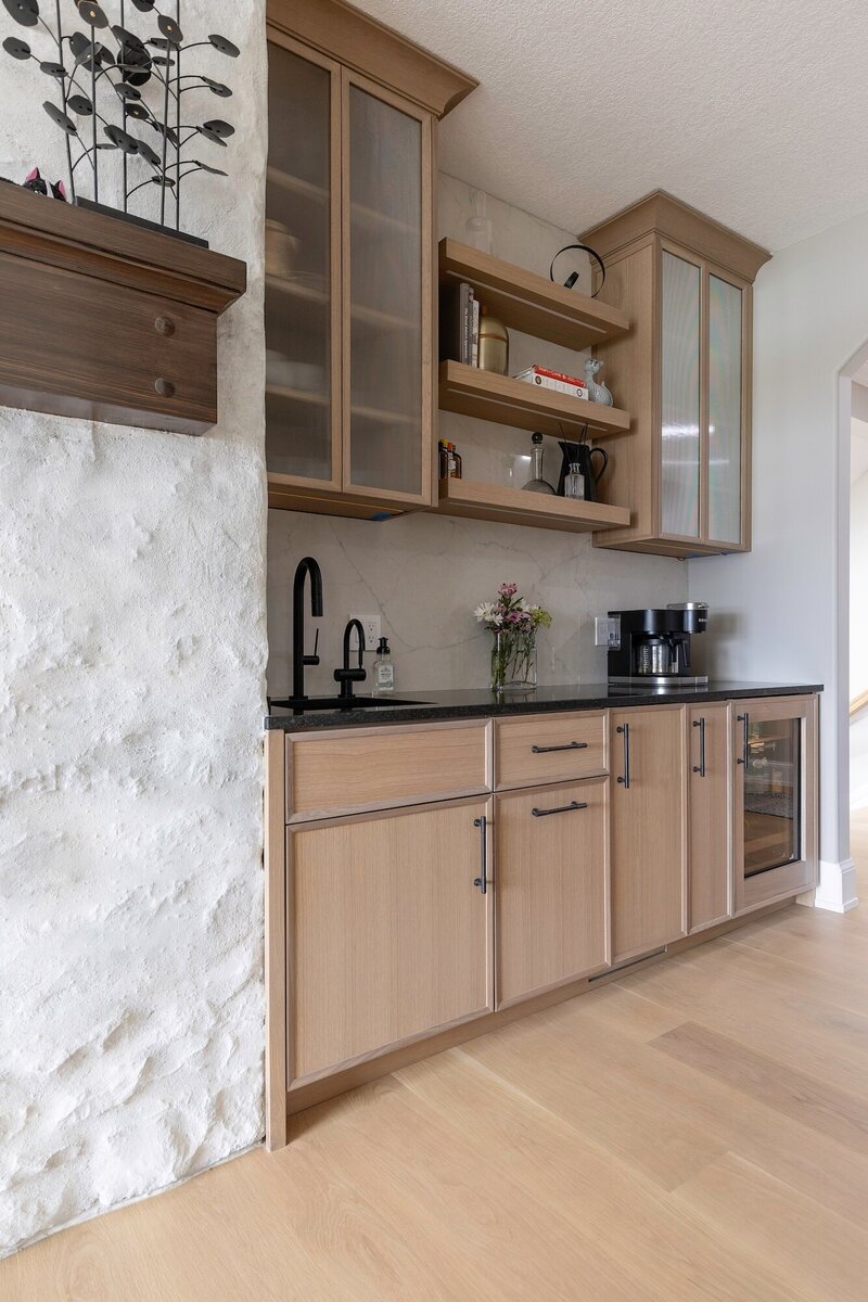 Modern wet bar with light wood cabinets and a textured wall.