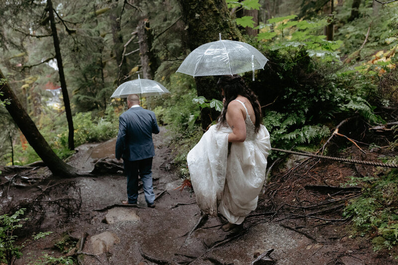 Couple holding umbrellas and walking in the woods.