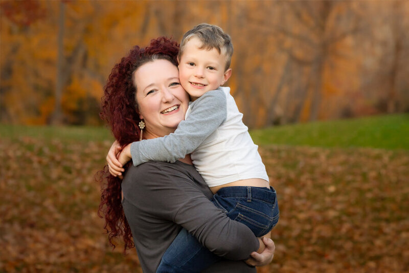 Mom and son hugging each other with fall colors and leaves in background.