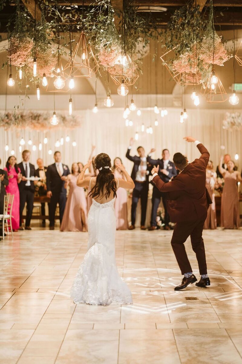 A joyful bride and groom dancing together during their reception, surrounded by friends and family.