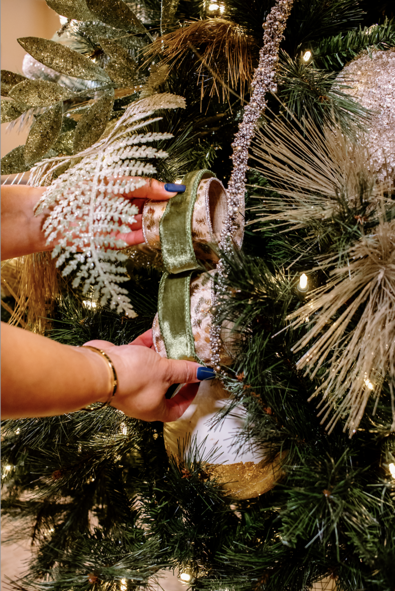 hands placing ribbon on a decorated Christmas tree
