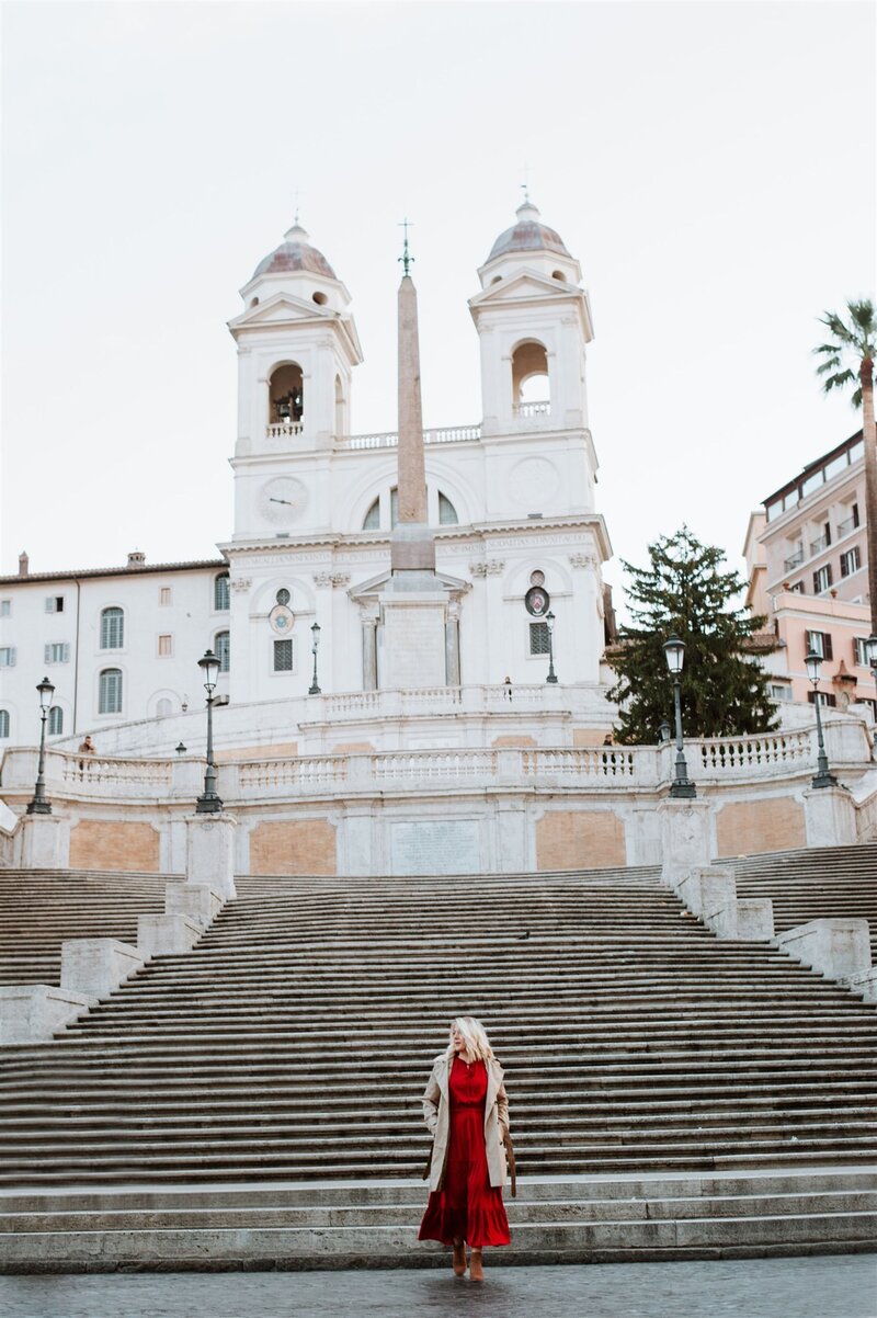 Traveler in a red dress standing in front of the historic Spanish Steps in Rome, Italy during golden hour.