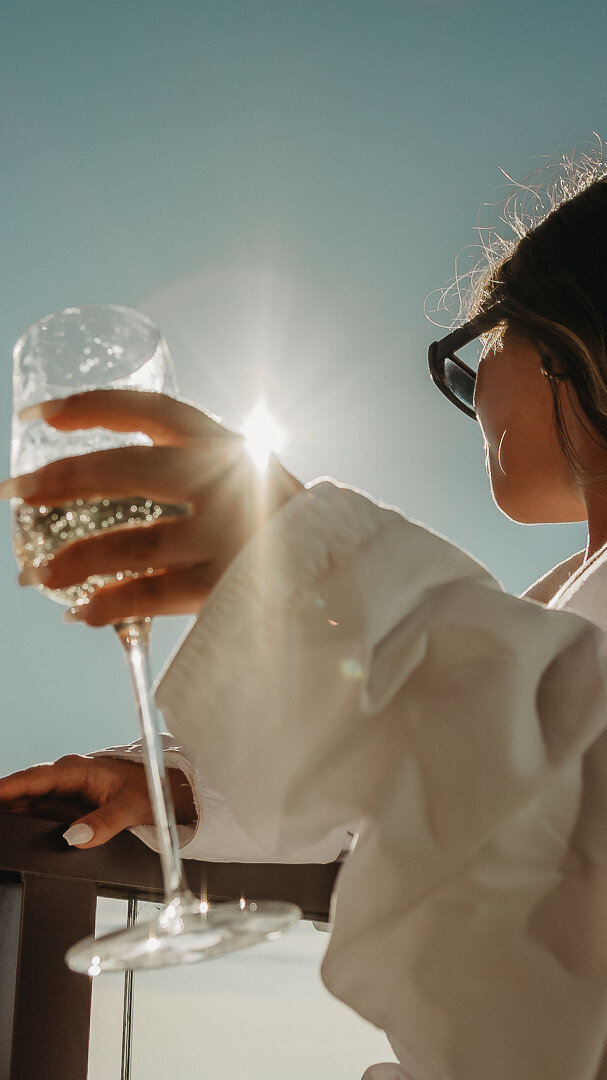 A woman in sunglasses holds her drink while looking at the sky