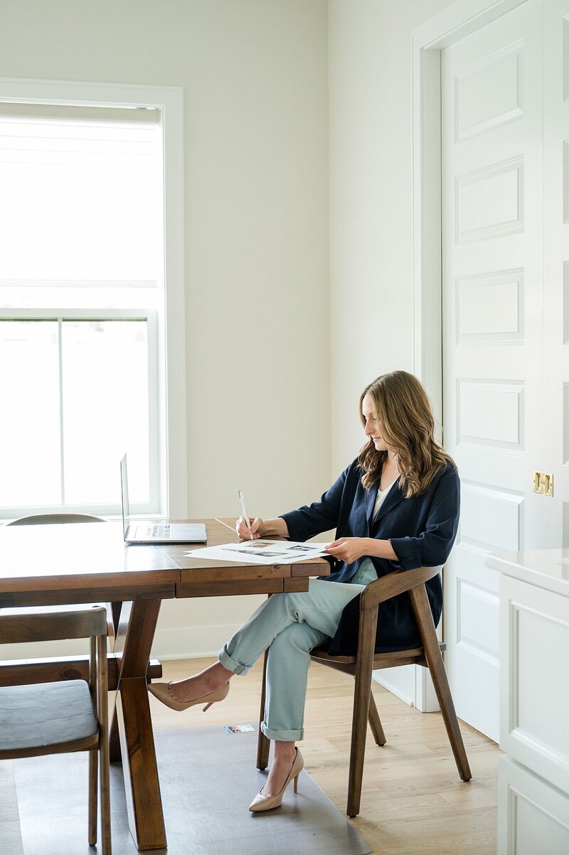 Columbus photographer sits at a dark wood desk in a dining room with her legs crossed as she outline a plan on paper for branding photos