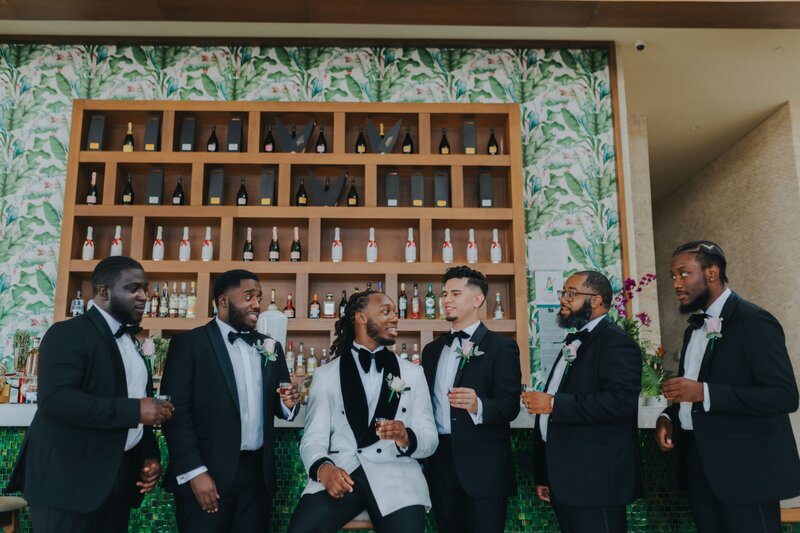 Groomsmen in tuxedos standing in front of a bar.