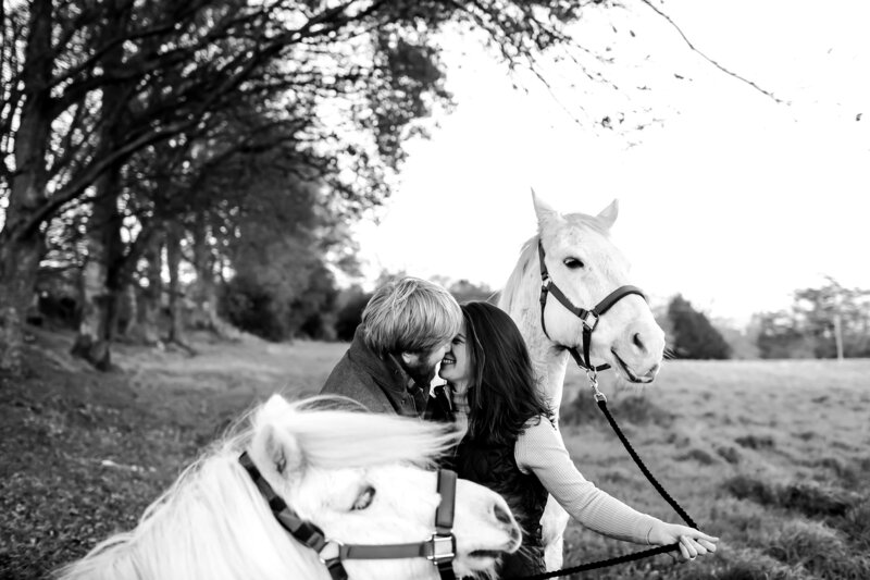 engagement-shoot-in-surrey-by-leslie-choucard-photography-couple-kissing-in-black-and-white-with-horses