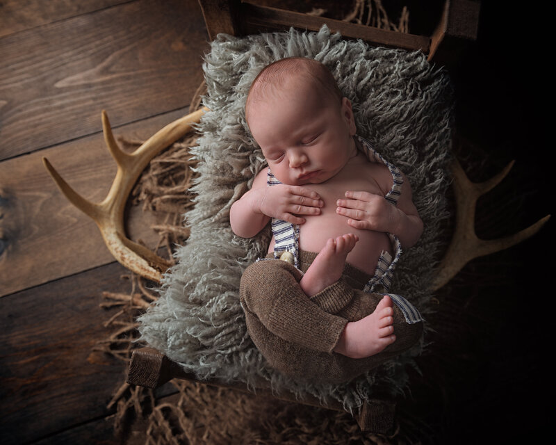 Blending rustic charm and vintage warmth, this newborn portrait features striped suspenders, antlers, and cozy textures.