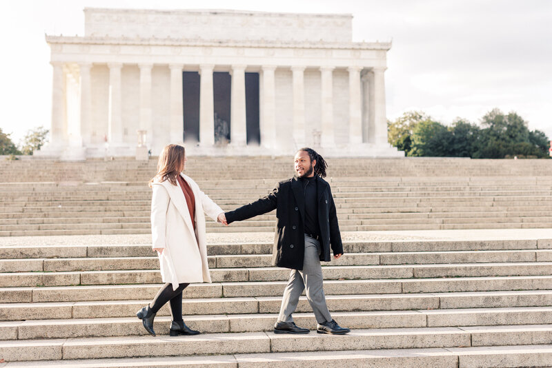 A couple holds hands as they walk the Lincoln Memorial for their engagement session