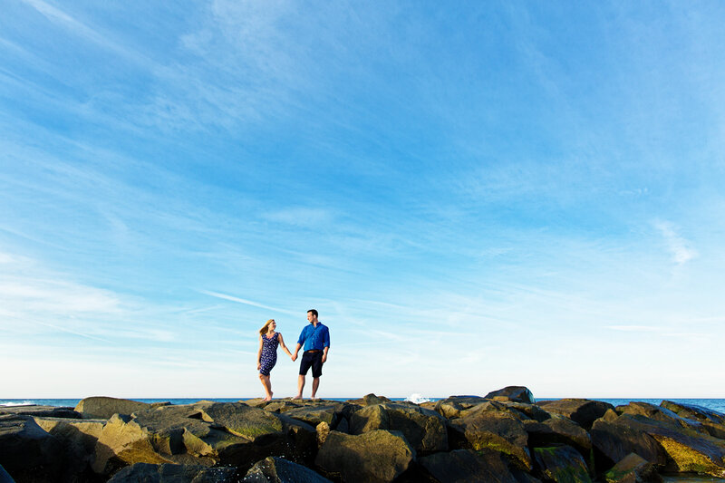 Couple standing together on a rock wall at the New Jersey Shore, celebrating their love during their destination engagement session.