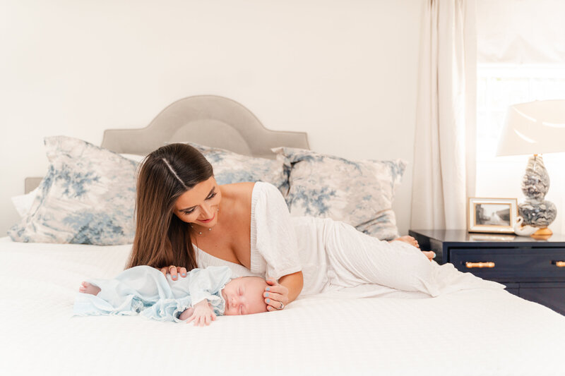 Mother cradles baby boy on white bed during newborn photography session in home lifestyle