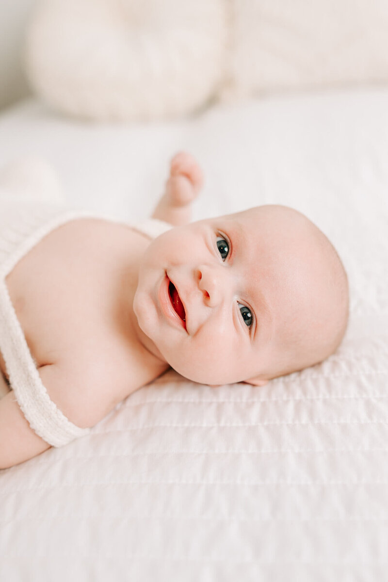 Baby boy laying in white overalls on the bed in the studio of molly berry photography