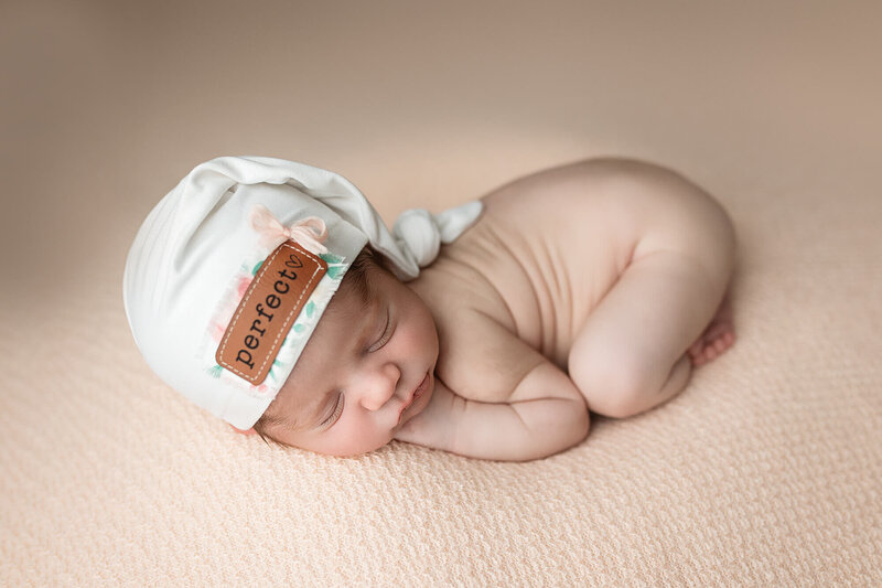 Newborn baby girl posed on a light pink backdrop for her newborn session.