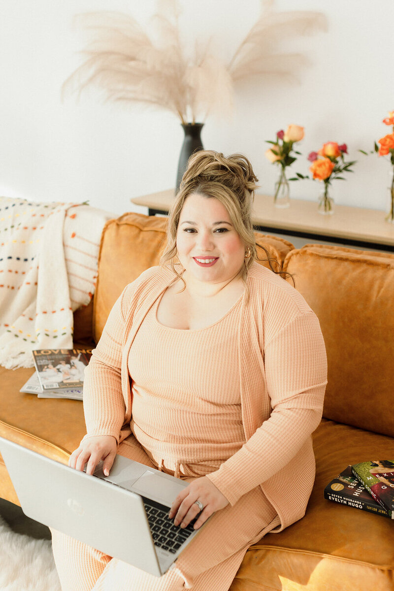 Cinthia Onines sitting down on a brown sofa with a laptop on her lap