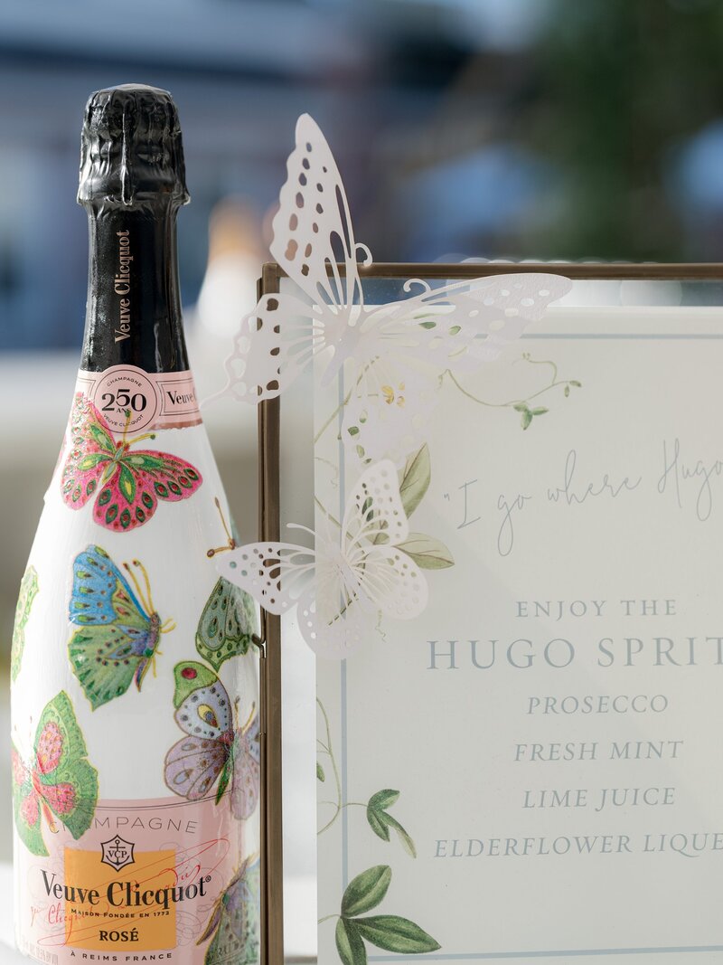 Bottle of sparkling wine with butterfly design next to a printed drink menu.