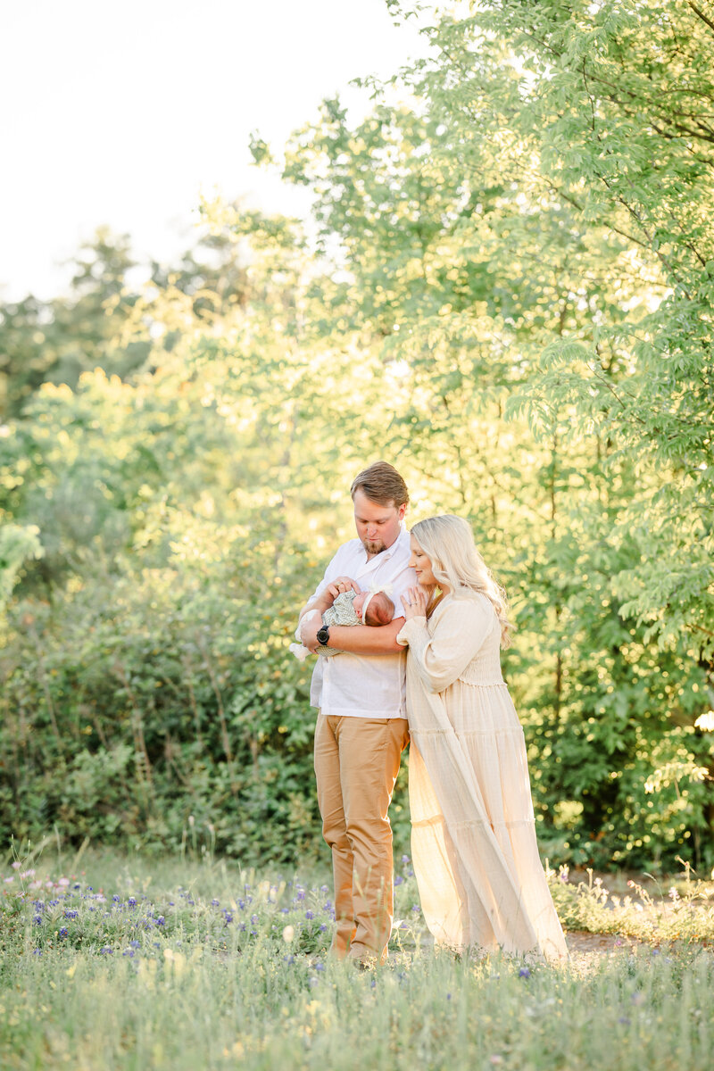 The family photo captures a serene and picturesque moment in a field of vibrant bluebonnets. Mom, dad, and their newborn baby stand together, basking in the warm glow of the setting sun. The lush, verdant field stretches out before them, creating a natural and organic backdrop that complements the family's casual, yet elegant attire.  The photographer, Bri Sullivan, has masterfully crafted a light and airy style, allowing the natural beauty of the scene to shine. The soft, diffused lighting casts a gentle, ethereal glow over the entire composition, creating a sense of tranquility and peace.  The family's expressions are filled with joy and love, as they gaze adoringly at their newest addition. The baby appears content and serene, adding to the overall sense of warmth and intimacy.  The forest backdrop, with its towering trees and lush foliage, provides a stunning contrast to the open field, creating a sense of depth and dimension. The combination of the vibrant bluebonnets, the warm sunset, and the natural setting results in a truly breathtaking and timeless image.  Overall, this family photo session captures the essence of spring, with its vibrant colors, soft lighting, and the pure, unadulterated joy of a new life. Bri Sullivan's skilled eye and artful approach have produced a stunning and memorable keepsake for this family to cherish for years to come.