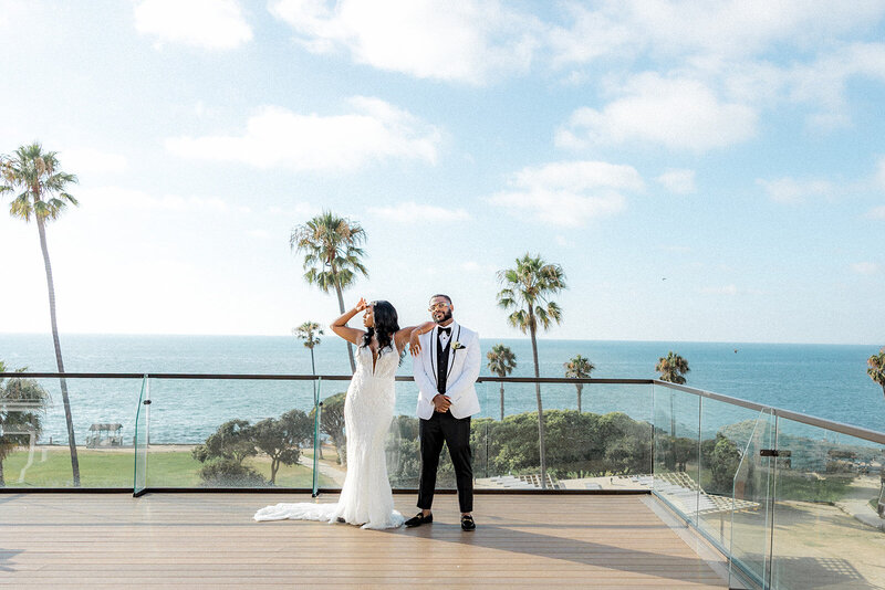 Bride and groom on balcony with the ocean and plam trees behind them in San Diego