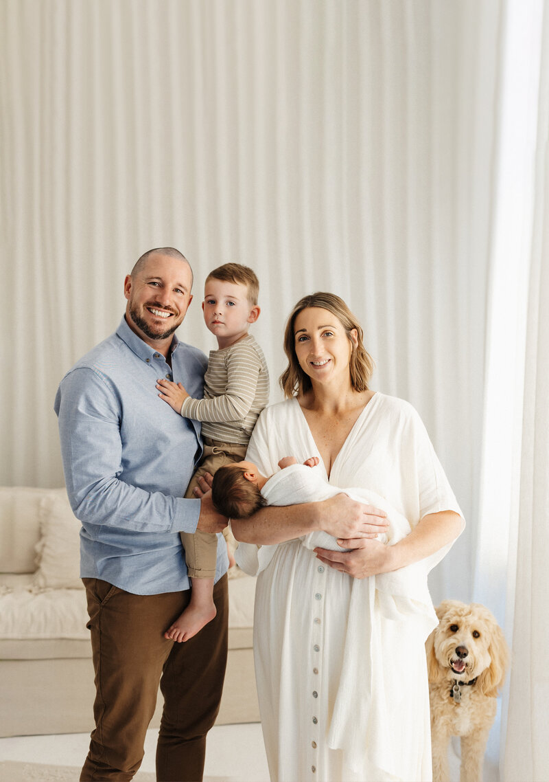 A family of four and their dog smile at the camera during a newborn photoshoot with lucy jane photography in christchurch
