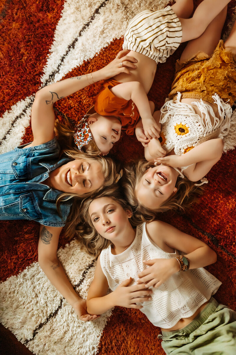 Mom lays on red and white retro carpet with her three kids during family session with Kansas City Lifestyle Photographer.