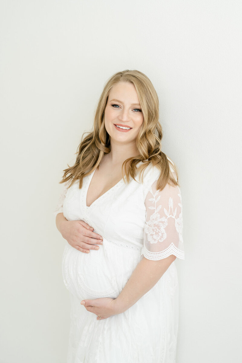 Mother wears white maternity dress during photo shoot at Julie Brock Photography studio in St Matthews KY