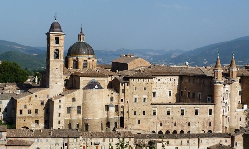 A panoramic view of Urbino, Italy, featuring the historic Ducal Palace and surrounding hills—one of the key destinations on the Wish You WERE Here Italy Tour with author Christy Schillig.