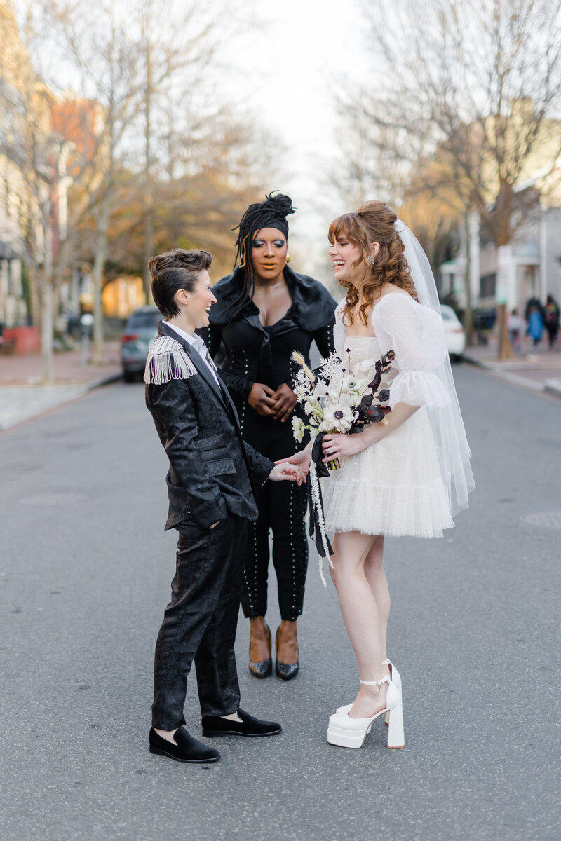 Black drag queen in a black jumpsuit officiating a nonbinary wedding couple in the middle of the street in Georgetown DC 