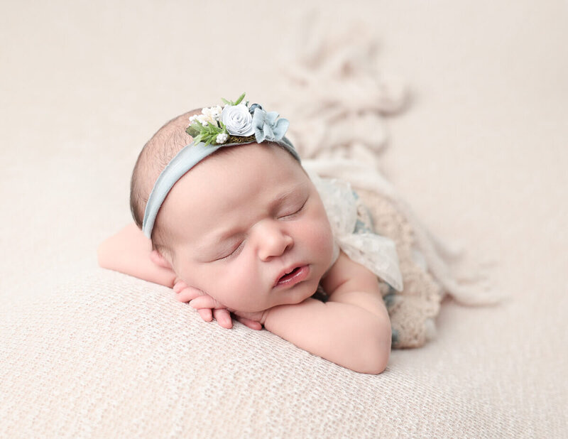 Newborn girl peacefully laying on a soft tan backdrop in a professional photography studio in Rochester, NY, capturing the essence of newborn photography.