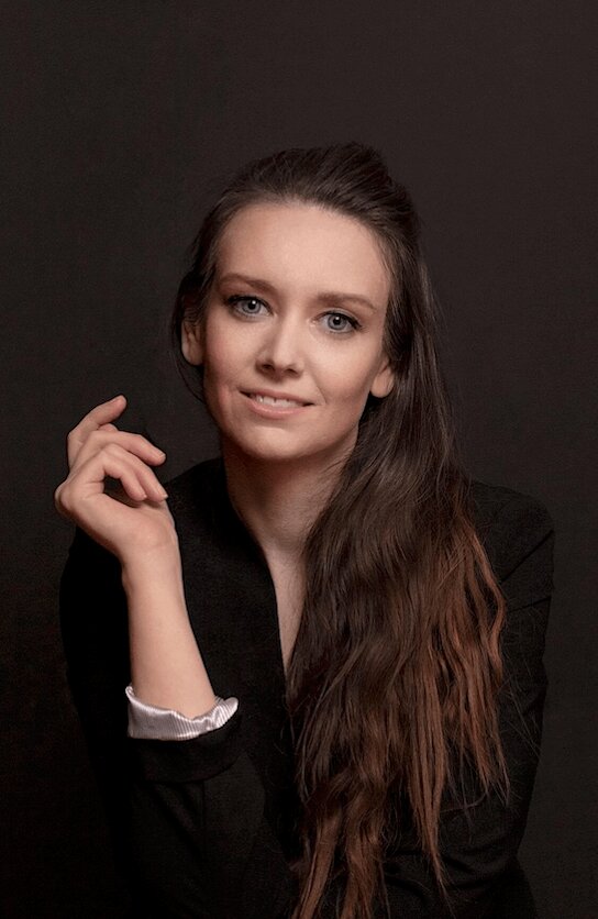 Self-Portrait slash headshot of Heather closeup smiling at the camera with a black blazer and black backdrop
