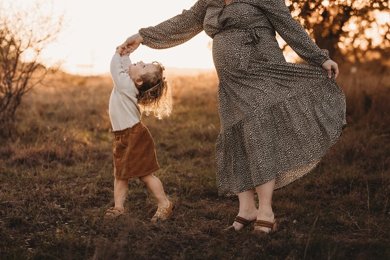 A little girl twirling while holding her mom's hand