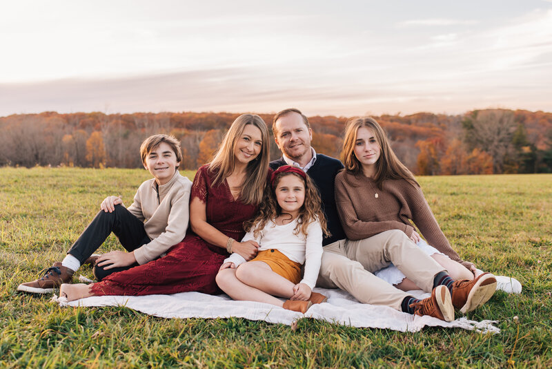 Family of five smiling at the camera at sunset in a field