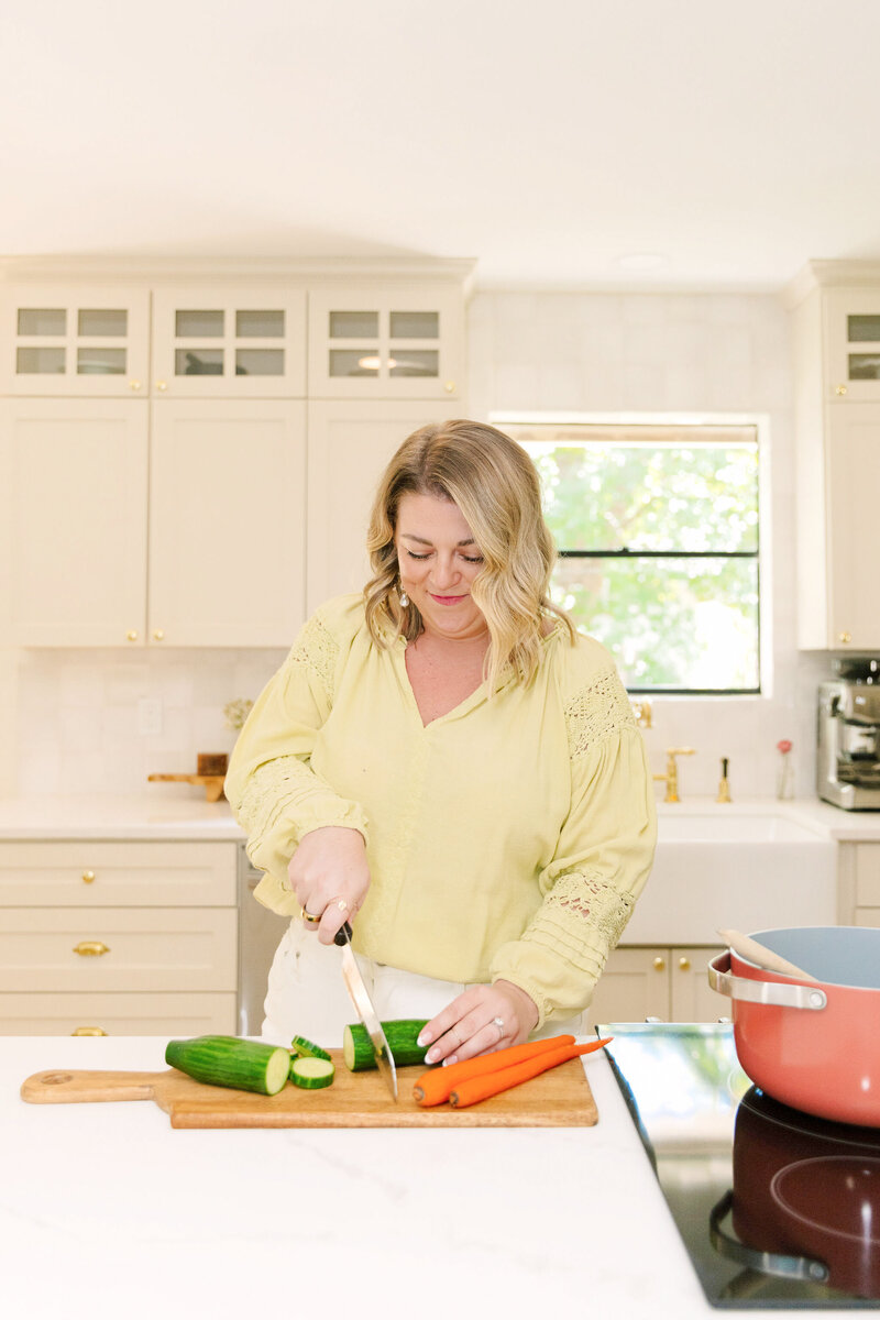 Mollie Mason in a green top cutting vegetables on a cutting board on her kitchen counter