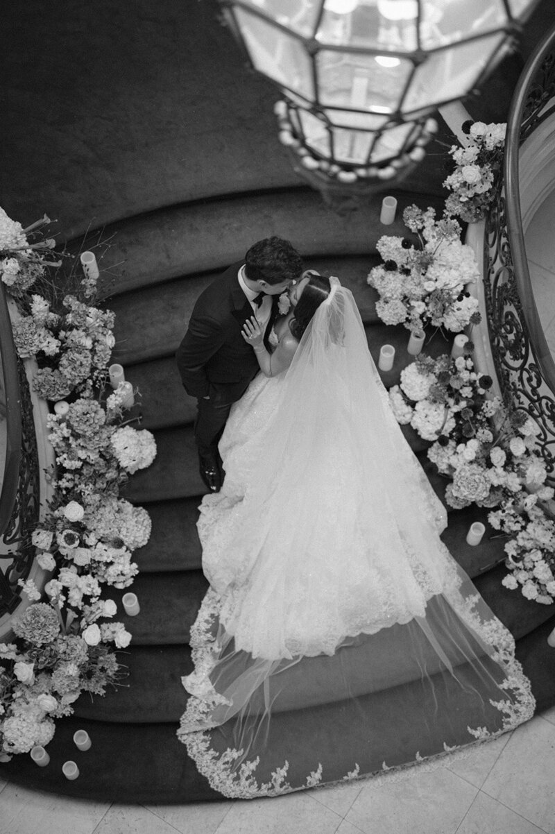 Kaitlyn and Chris on a staircase lined with white florals, in black and white