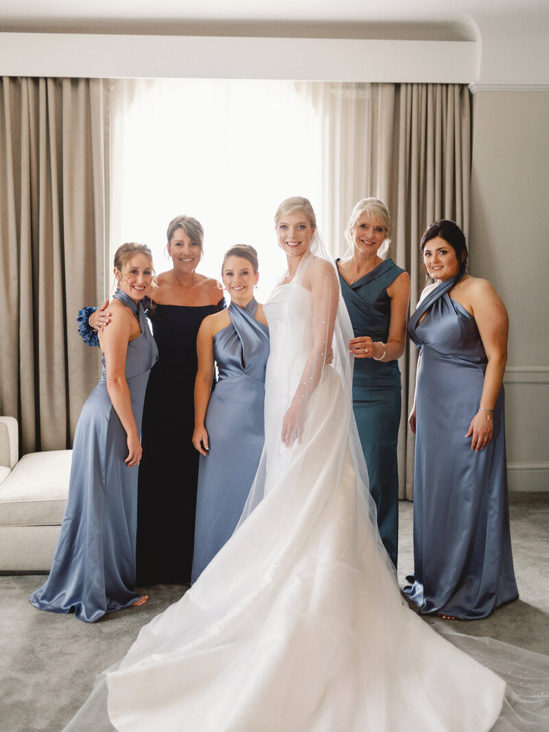 Modern bride with her mom, future mother in law, bridesmaids while wearing her gown and veil