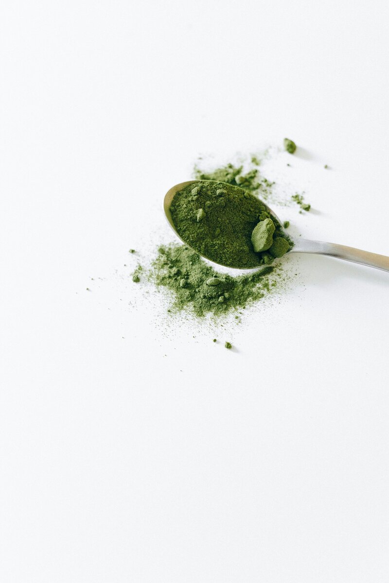 Spoon full of green powder sitting on a white surface