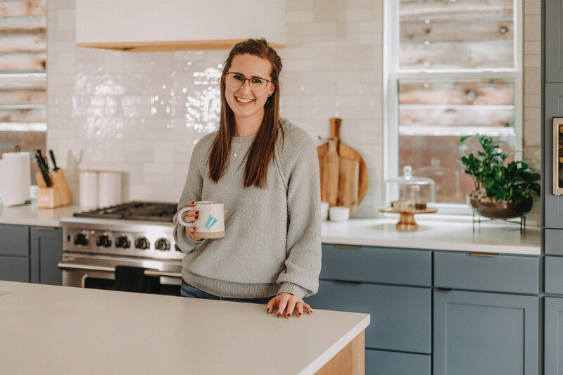 Liz Strong Studio Manager smiling at camera in kitchen with mug in hand