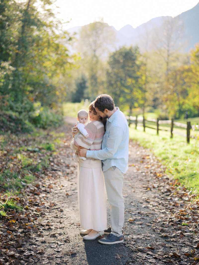 A father hugging his spouse and newborn son at a park in Squamish