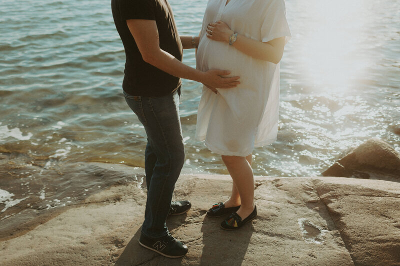 Pari seisoo rantakalliolla ja mies pitelee kättä raskaana olevan vaimon vatsalla Espoossa Karhusaaressa Espoossa