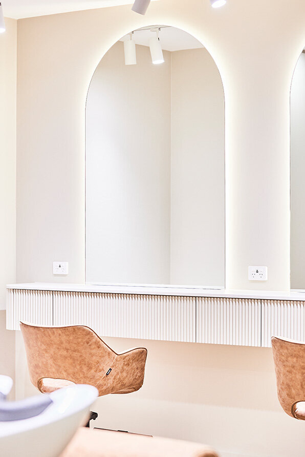 Modern salon station featuring arched mirrors, beige styling chairs, and soft ambient lighting in Sydney CBD.